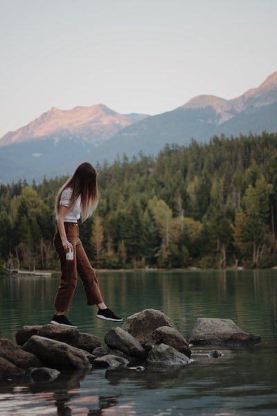 女人踩灰色岩石山湖附近观看白天
